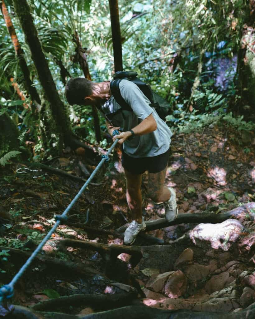 Hiker using fixed safety ropes to climb steep and muddy jungle terrain on The Lost Waterfalls trail in Boquete Panama